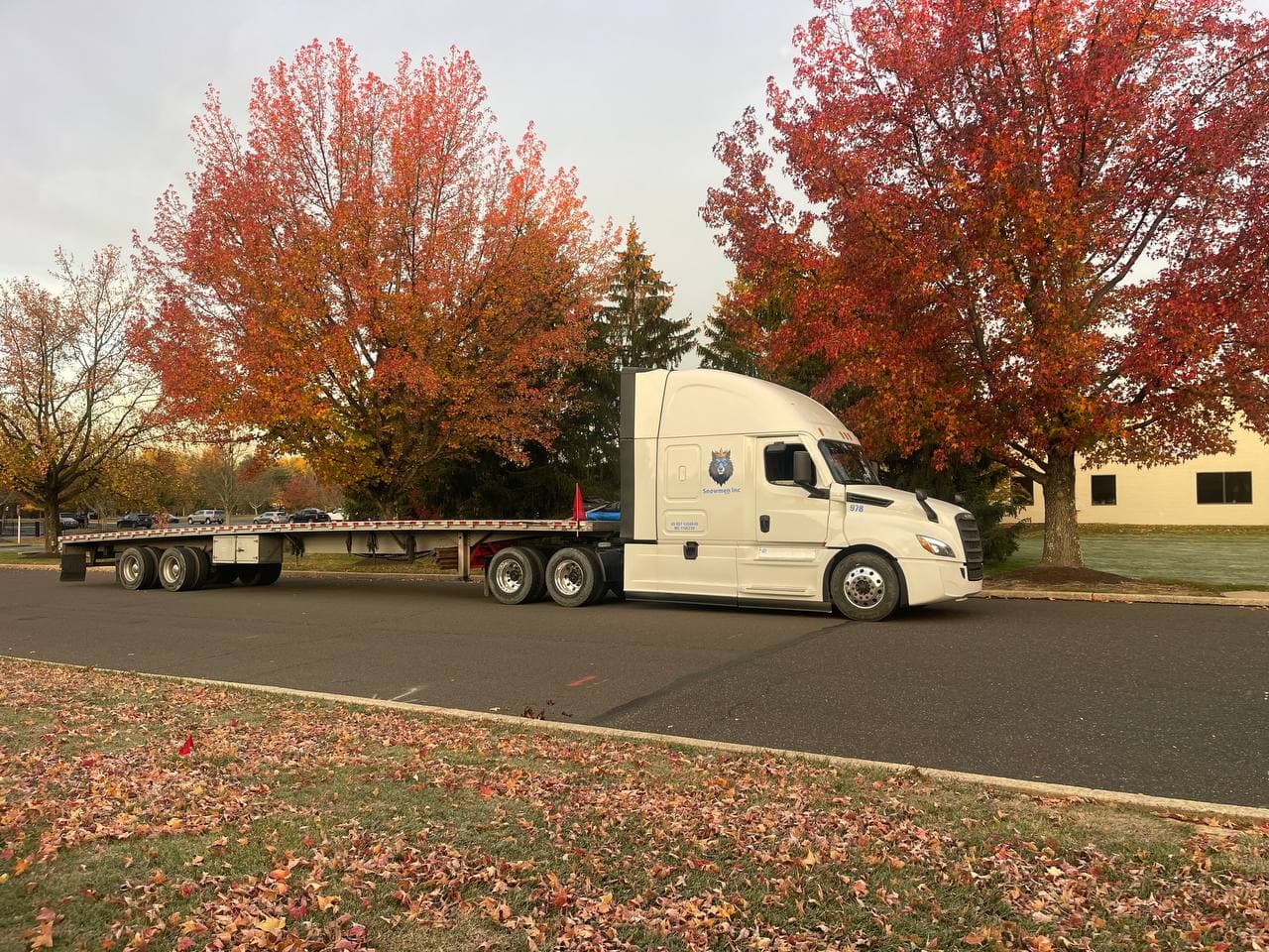 White Snowmen Express truck with flatbed trailer parked under brilliant autumn foliage