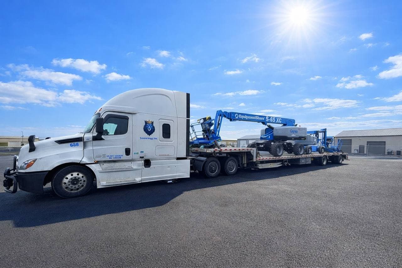 Snowmen Express truck 688 hauling a Genie S-65 XC boom lift under clear blue skies