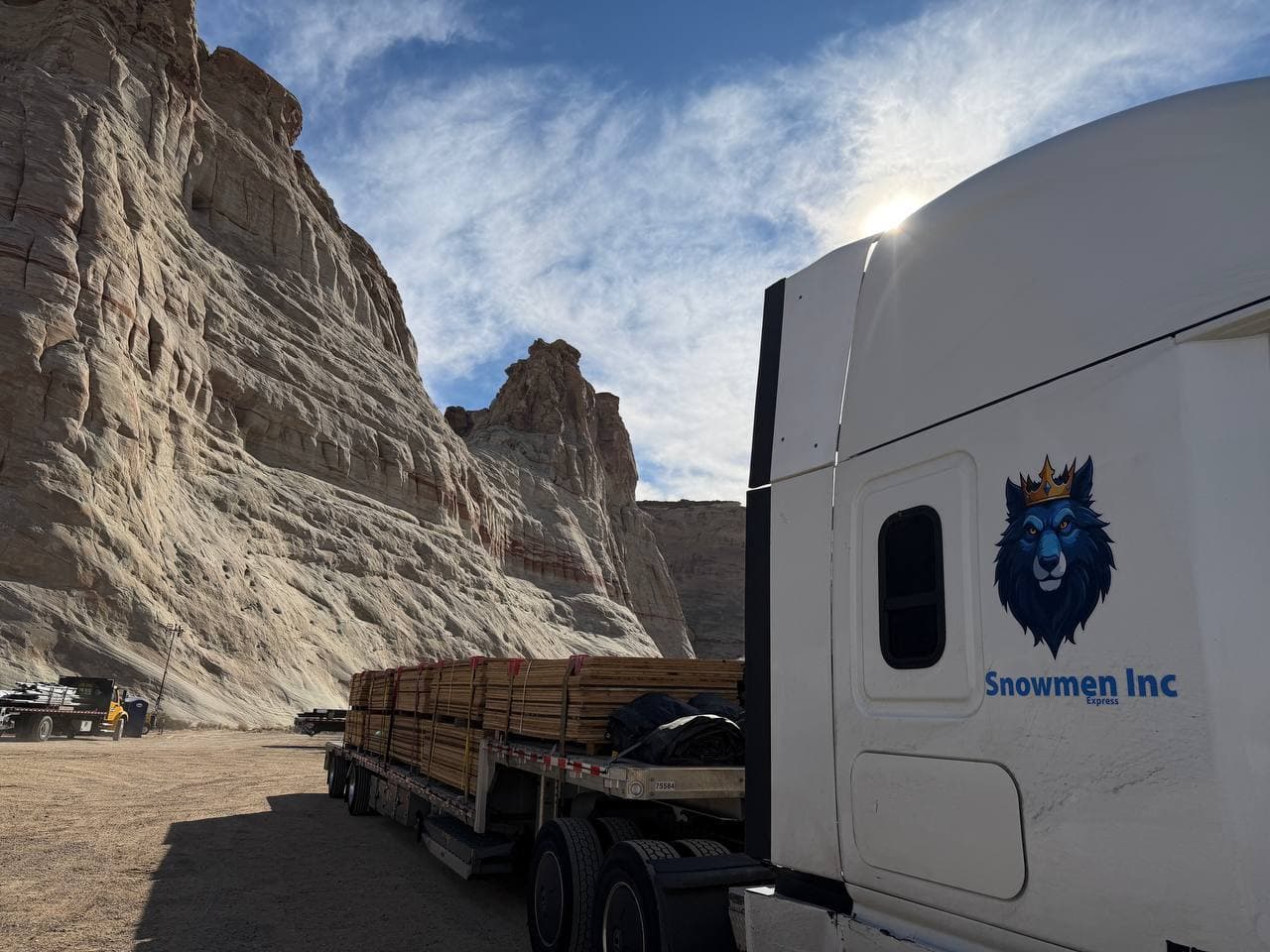 Snowmen Express truck displaying the blue wolf with crown logo, parked at a dramatic white rock canyon in the American Southwest