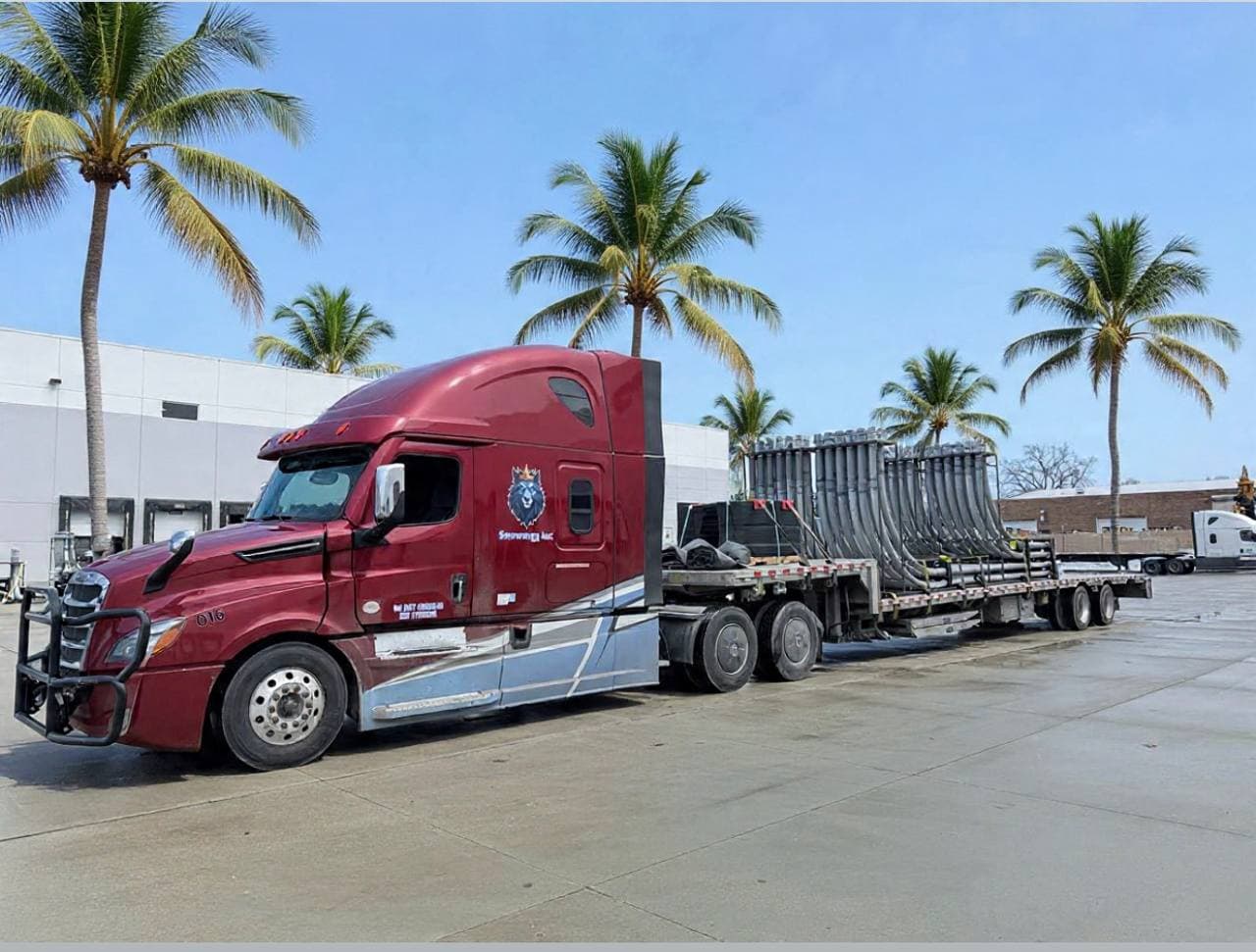 Red Snowmen Express truck with flatbed cargo parked near palm trees