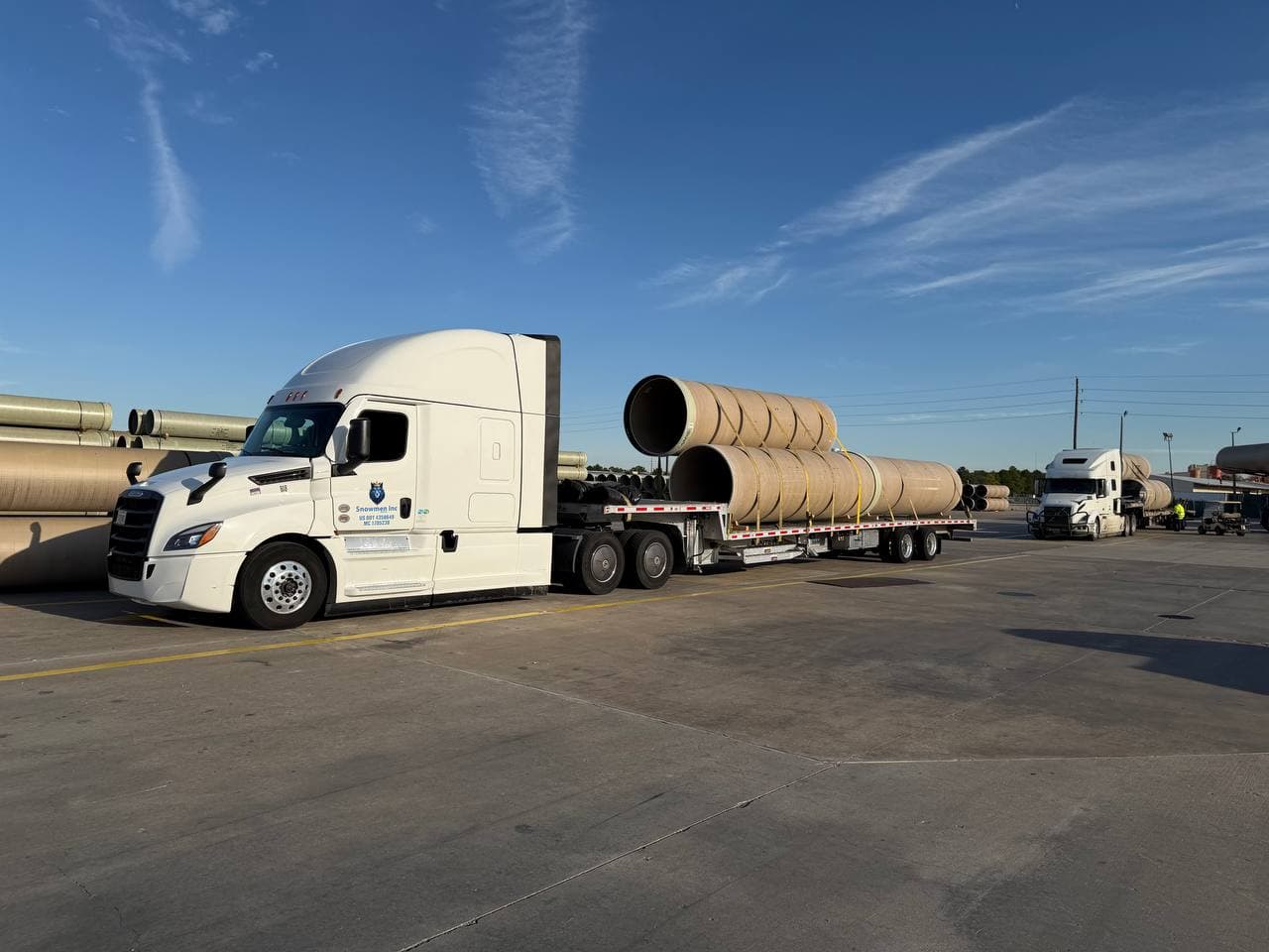 Snowmen Express truck hauling large concrete pipe cylinders at a construction staging area